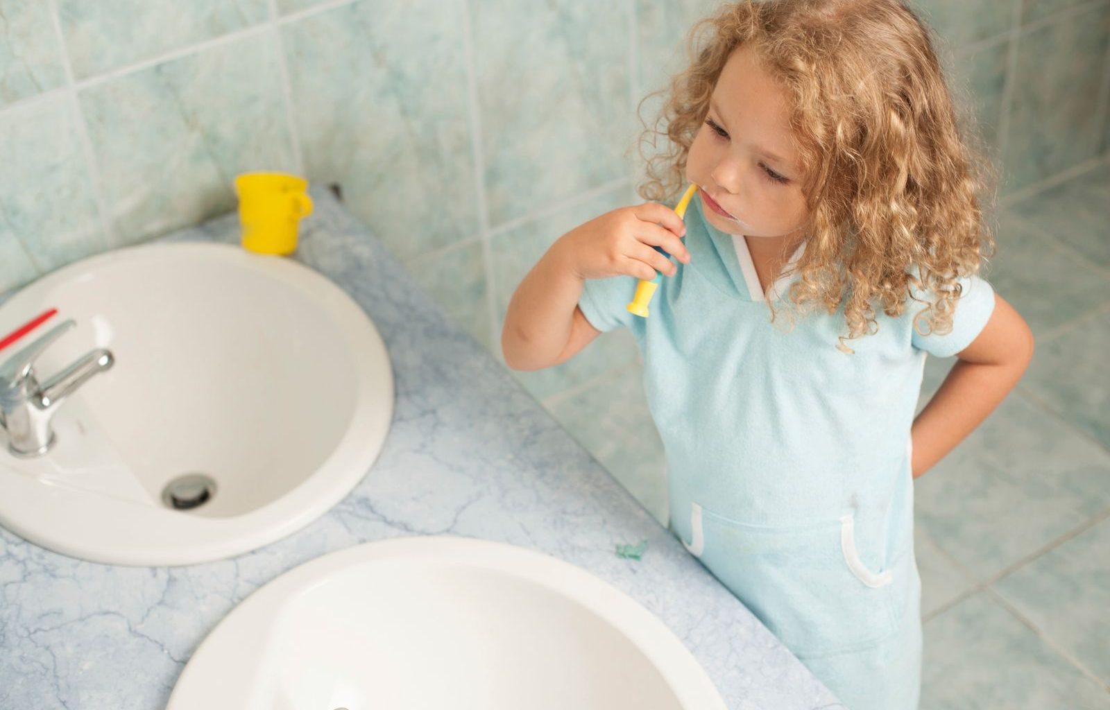 Child brushing teeth by sink, highlighting personal hygiene habits.