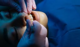 A dentist examines a patient's teeth during a dental procedure under bright clinic lights.