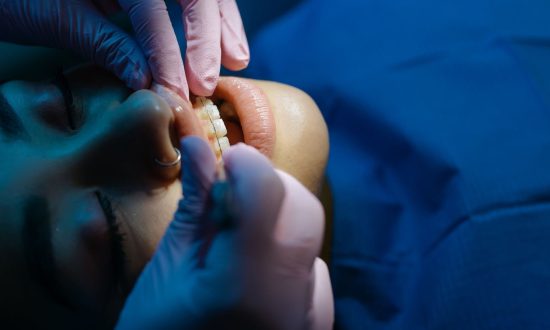 A dentist examines a patient's teeth during a dental procedure under bright clinic lights.
